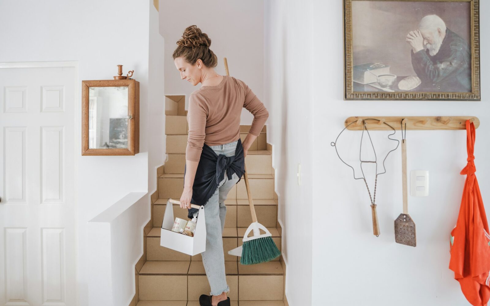 Personne montant un escalier avec un panier de produits et un balai